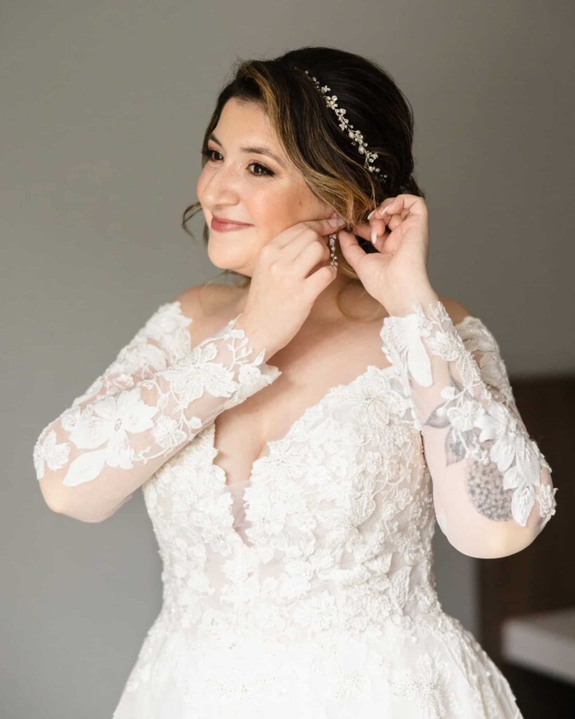 Bride smiling while she puts on her earring. 