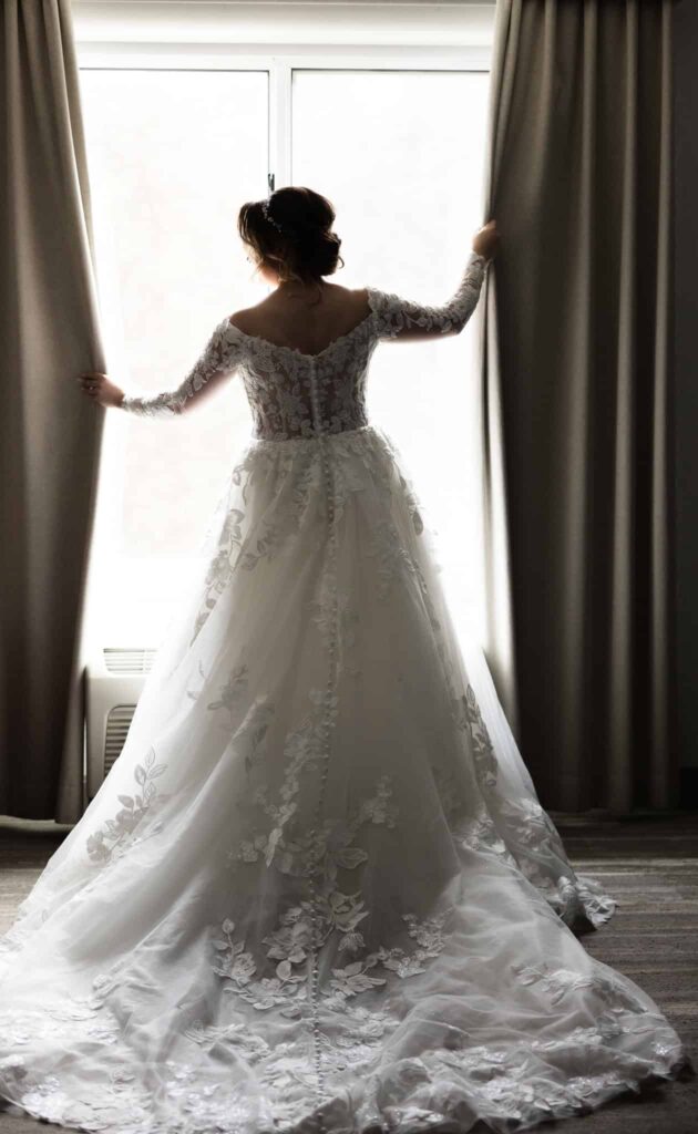 Bride in the window of the hotel room holding onto curtain.