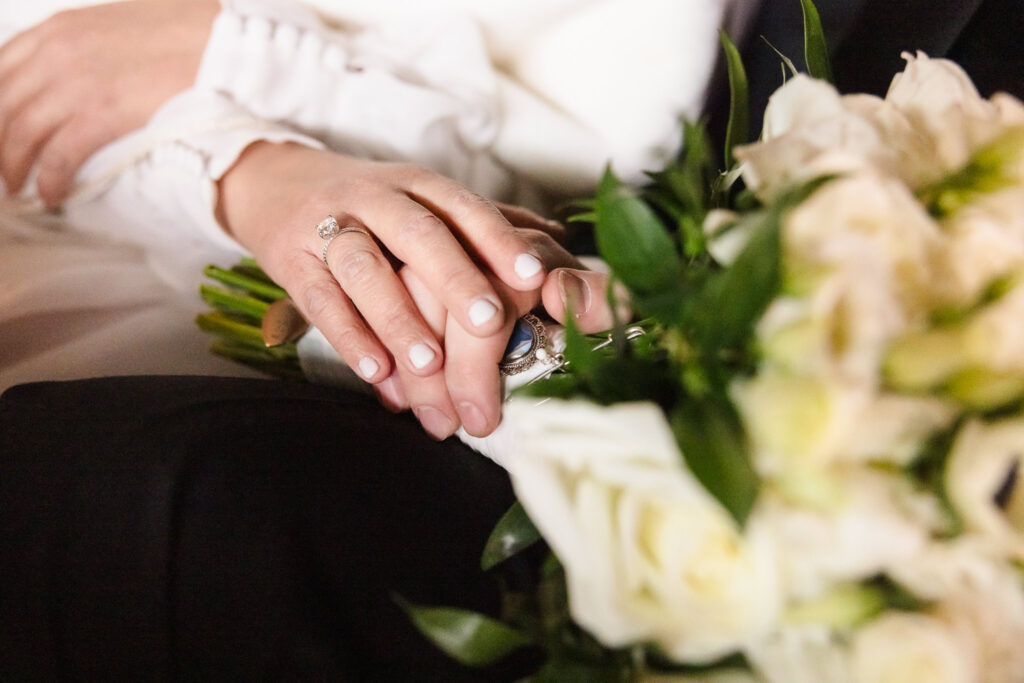 Hands of bride and groom on bouquet at Inn at New Hyde Park.