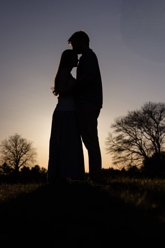 Silhouetted kiss at sunset with trees and garden backdrop — a perfect final frame.