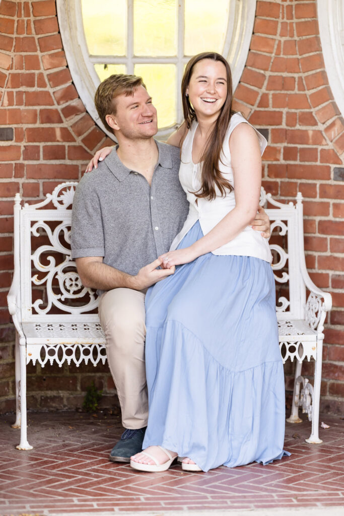 Fiancée leaning into her partner with eyes closed, seated on a garden bench at Old Westbury Gardens.