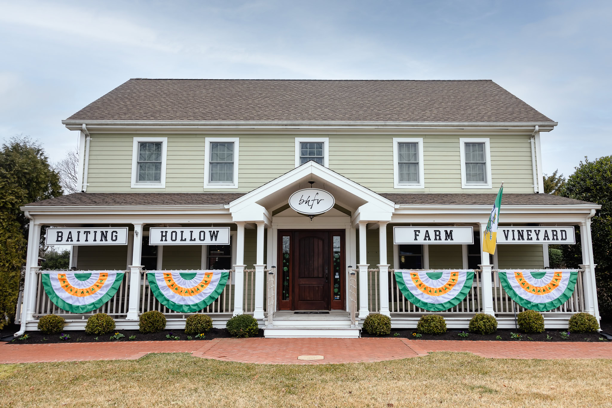 Front entrance of Baiting Hollow Farm Vineyard, featuring classic farmhouse architecture with festive green, white, and orange bunting decor.