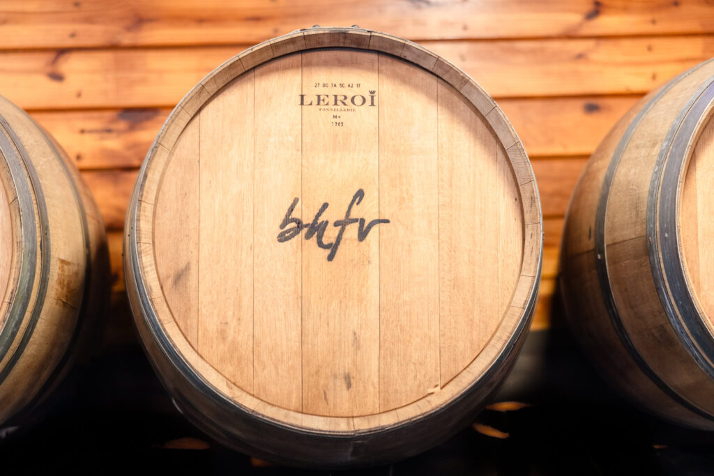 Close-up of a wine barrel marked with ‘bhfv’ at Baiting Hollow Farm Vineyard, set against a warm wooden wall.