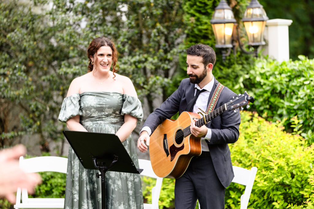 Live musicians performing at a spring wedding ceremony at The Briarcliff Manor, including a vocalist in a green floral gown and a guitarist in a suit.