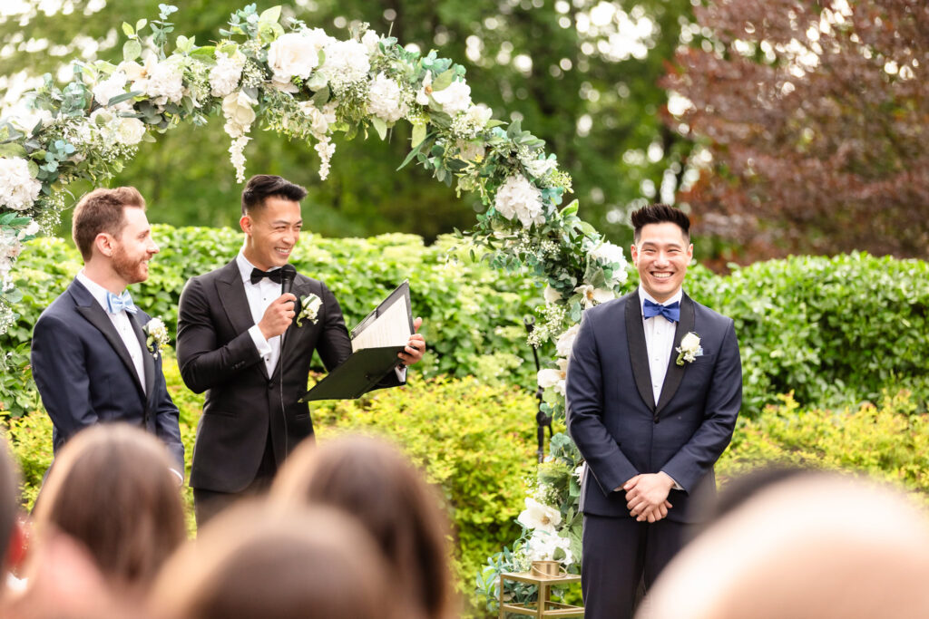 Groom reads heartfelt vows to his partner during their outdoor ceremony at The Briarcliff Manor, under a floral arch.
