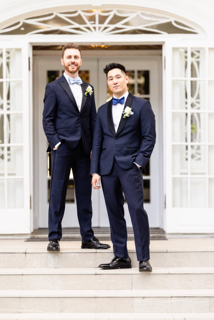 Grooms standing together on the front steps of The Briarcliff Manor, smiling confidently on their wedding day.