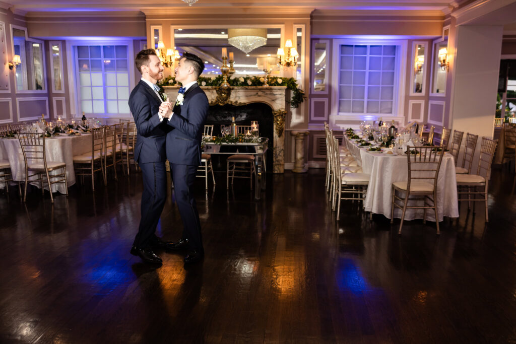 Grooms share their first dance in the candlelit ballroom at The Briarcliff Manor, surrounded by elegant tables and soft uplighting.