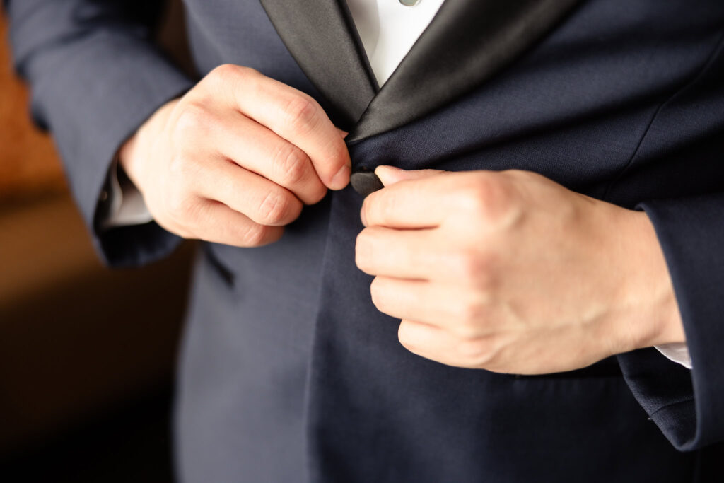 Close-up of a groom buttoning his tuxedo jacket, preparing for the ceremony at The Briarcliff Manor.