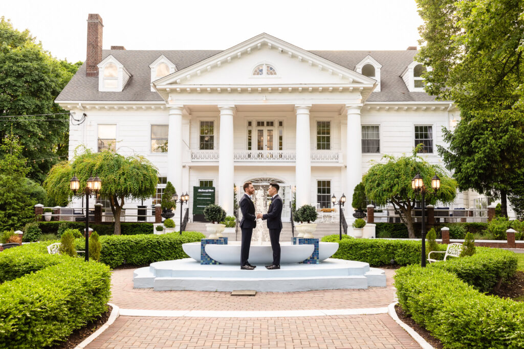 Groom and groom sharing a quiet moment in front of the fountain at The Briarcliff Manor, framed by the estate’s grand white-columned facade.