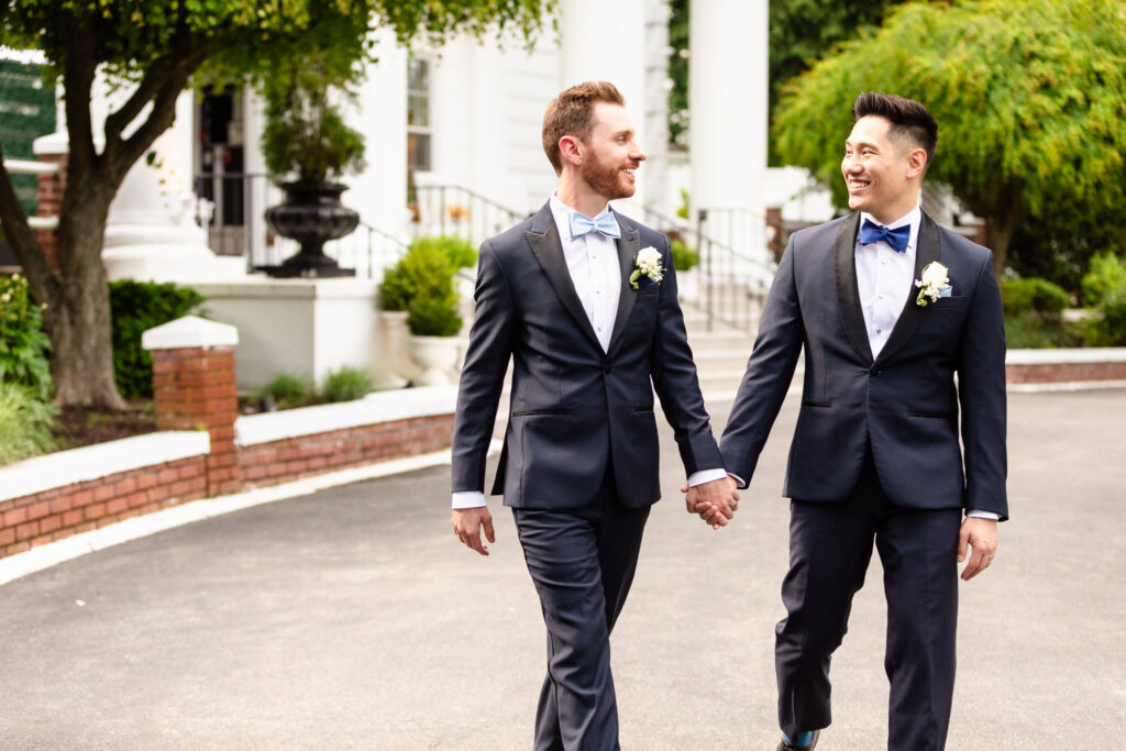 Groom and groom walking hand-in-hand outside The Briarcliff Manor, smiling at each other in front of the estate’s elegant white columns.