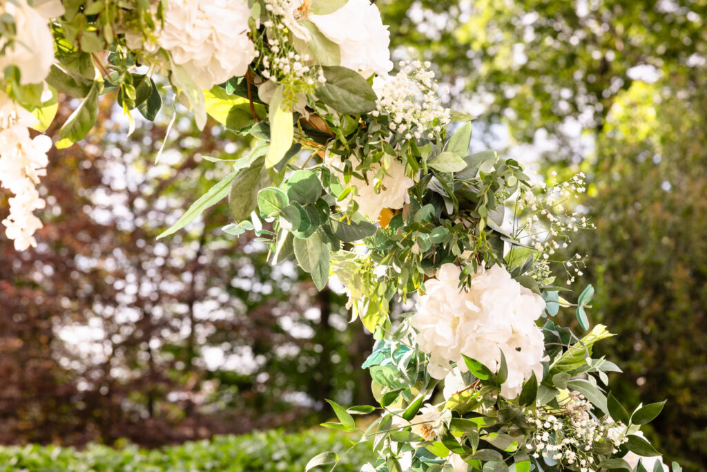 Close-up of a floral arch detail with white hydrangeas and soft greenery, glowing in afternoon light.