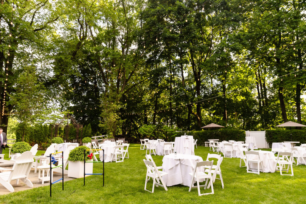 Outdoor cocktail hour setup at The Briarcliff Manor with white tables and chairs, surrounded by tall trees and garden greenery.