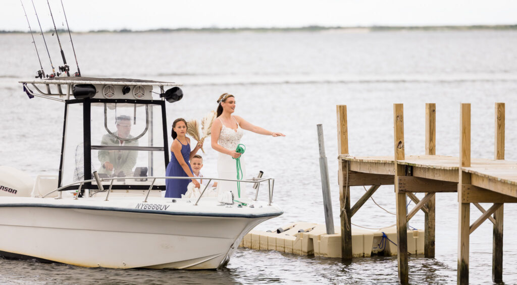Bride and bridal party arriving by boat, with the bride joyfully tossing flowers toward the dock.