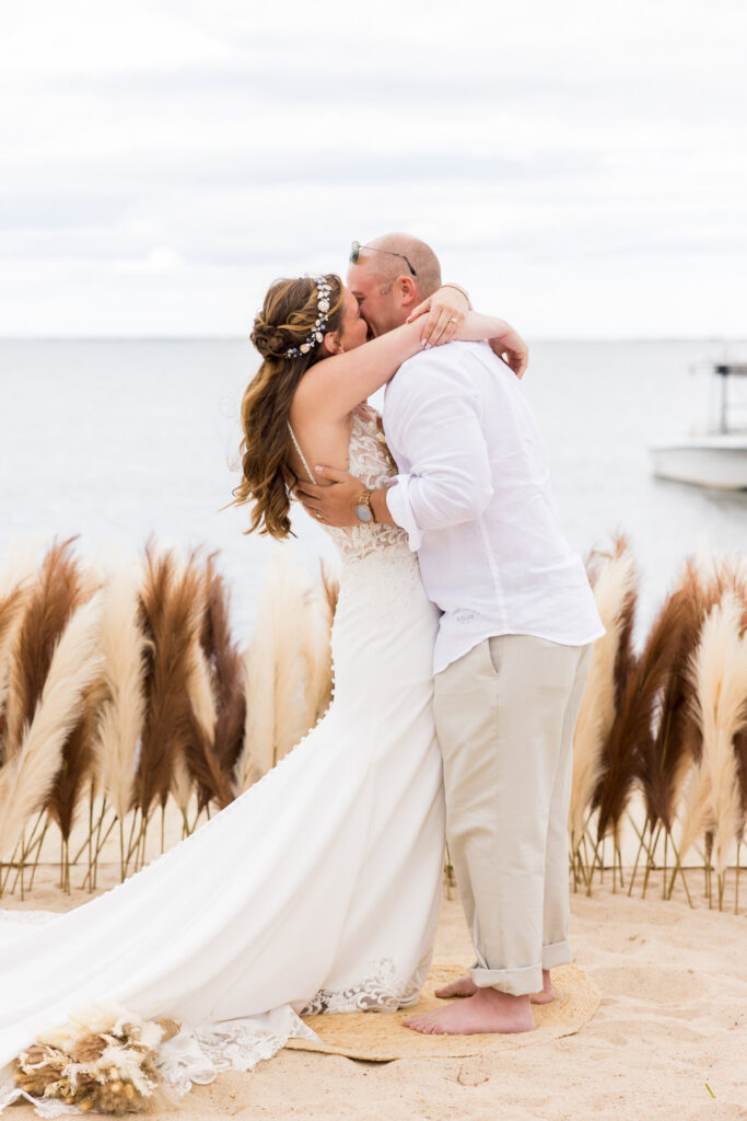 Bride and groom embracing after their ceremony on the sand, framed by pampas grass.