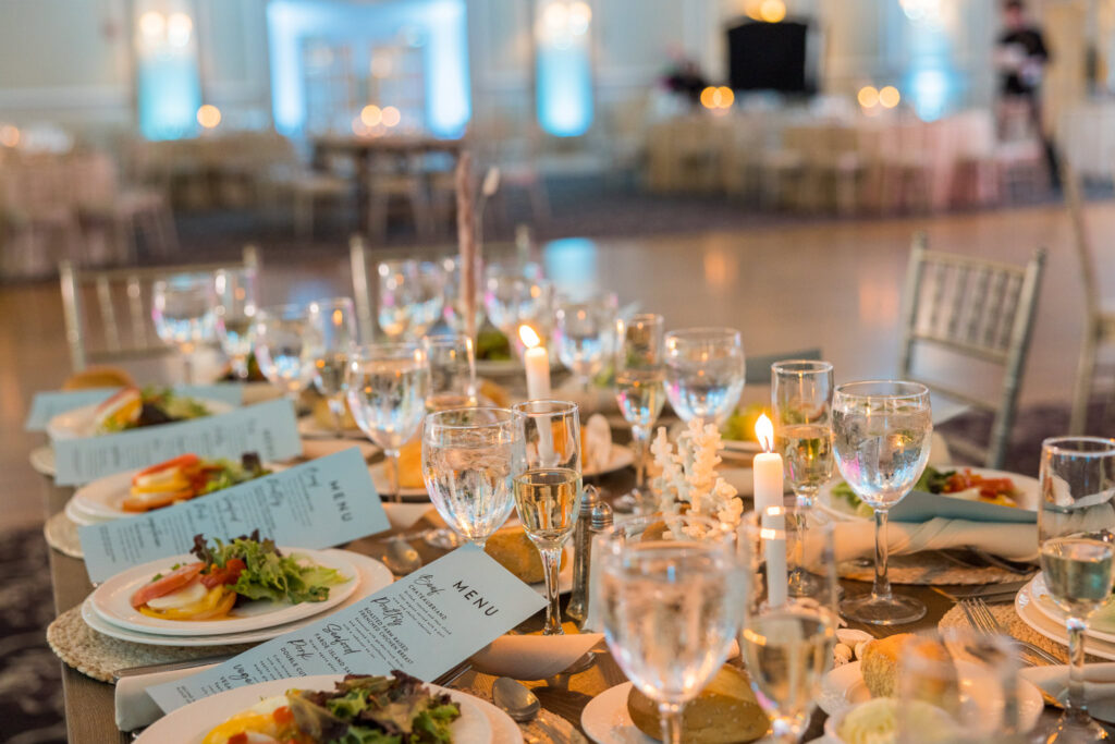 Candlelit reception table adorned with place settings, menus, and fresh salads.