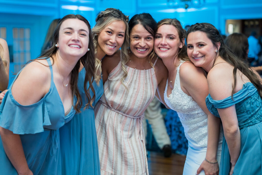 Group of wedding guests smiling and posing in soft blue and neutral dresses.
