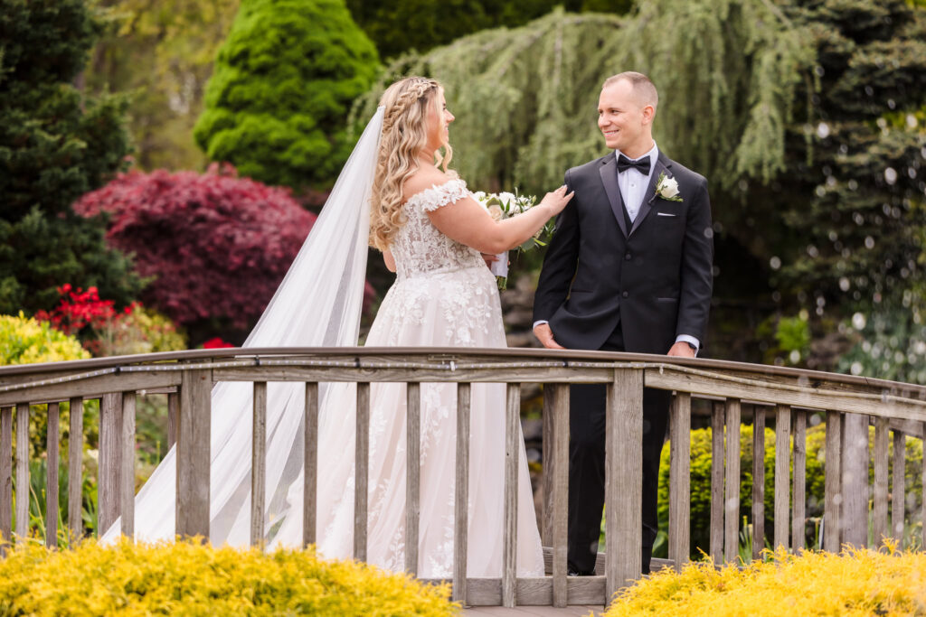 Bride and groom share a joyful first look on a wooden garden bridge surrounded by vibrant spring foliage at East Wind Long Island.

