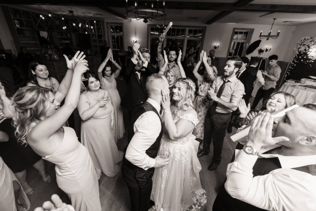Bride and groom share a kiss on the dance floor surrounded by cheering guests during a joyful wedding reception at East Wind Long Island.

