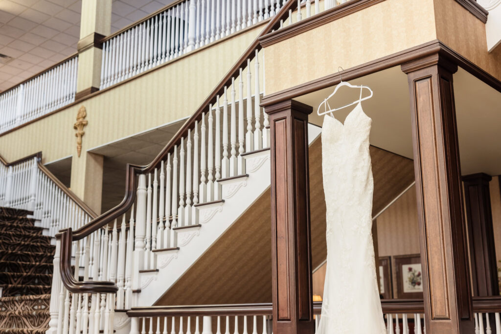Lace wedding gown hangs gracefully on a staircase railing at East Wind Long Island, ready for the day’s celebration.

