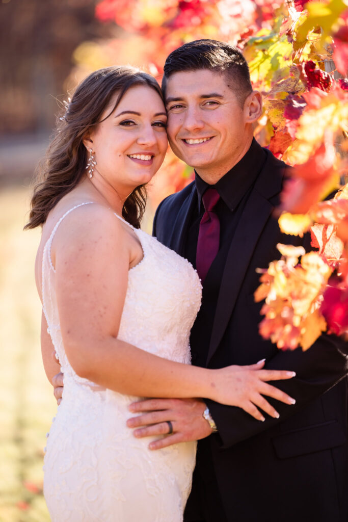 Bride and groom embrace amid vibrant autumn foliage in the vineyard at East Wind Long Island, glowing with golden-hour light.

