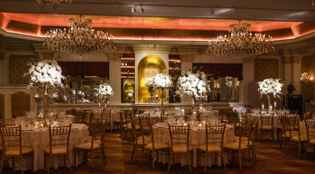 The Grand Ballroom at the Garden City Hotel styled for a luxurious wedding reception, featuring crystal chandeliers, dramatic uplighting, gold chiavari chairs, and lavish floral centerpieces—an iconic setting for elegant Long Island weddings.