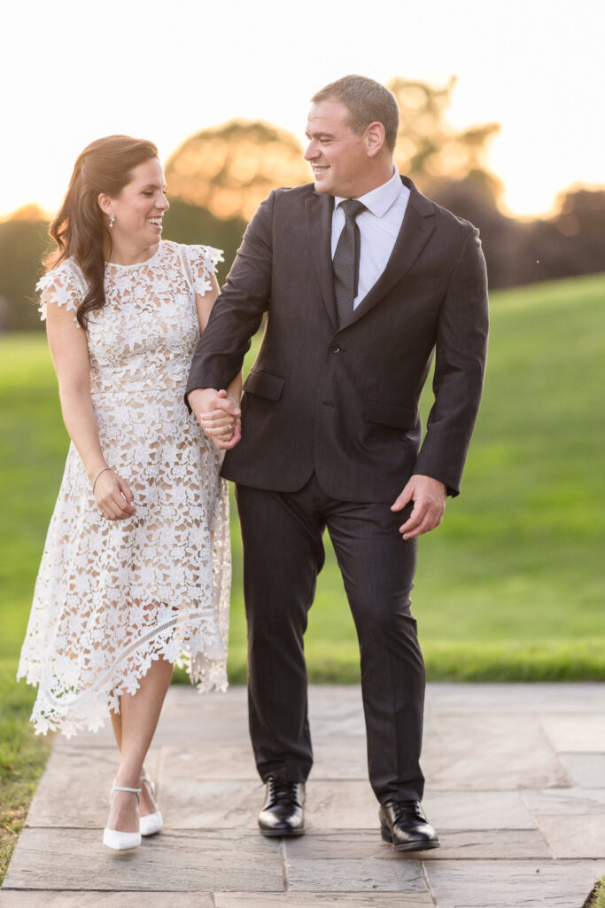 Couple walking hand-in-hand along a stone path at Glen Head Country Club, sharing a joyful moment at sunset.