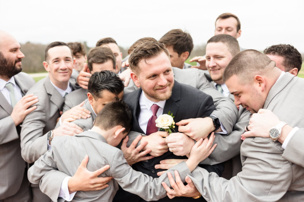 Playful group hug as the groomsmen surround the groom, sharing laughter and excitement before the wedding ceremony.