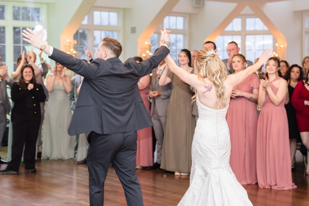 Bride and groom twirling on the dance floor as guests cheer during their first dance at The Heritage Club reception.