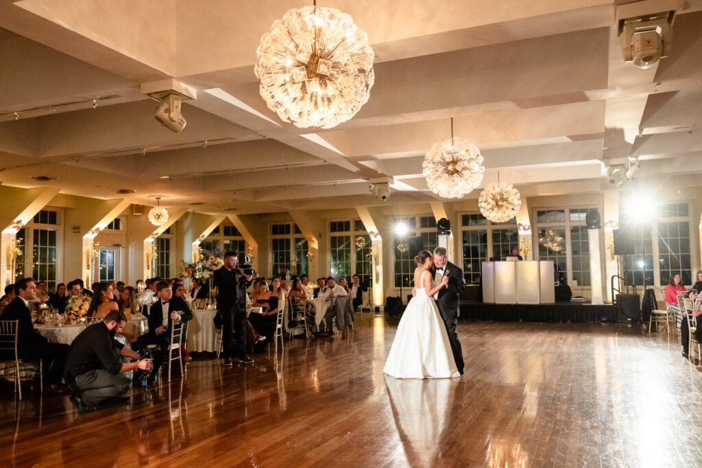 Bride and groom share their first dance beneath glowing chandeliers in the Grand Ballroom at The Heritage Club at Bethpage.