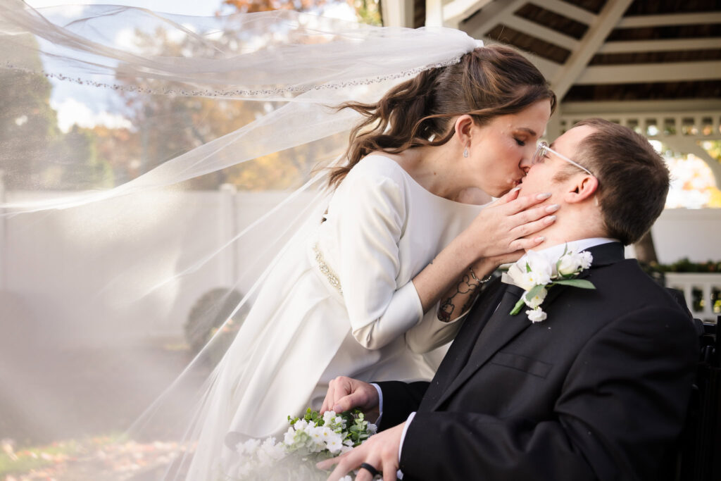 Bride and groom share a tender kiss under the bride’s flowing veil at their fall wedding at Fox Hollow Winter Garden.