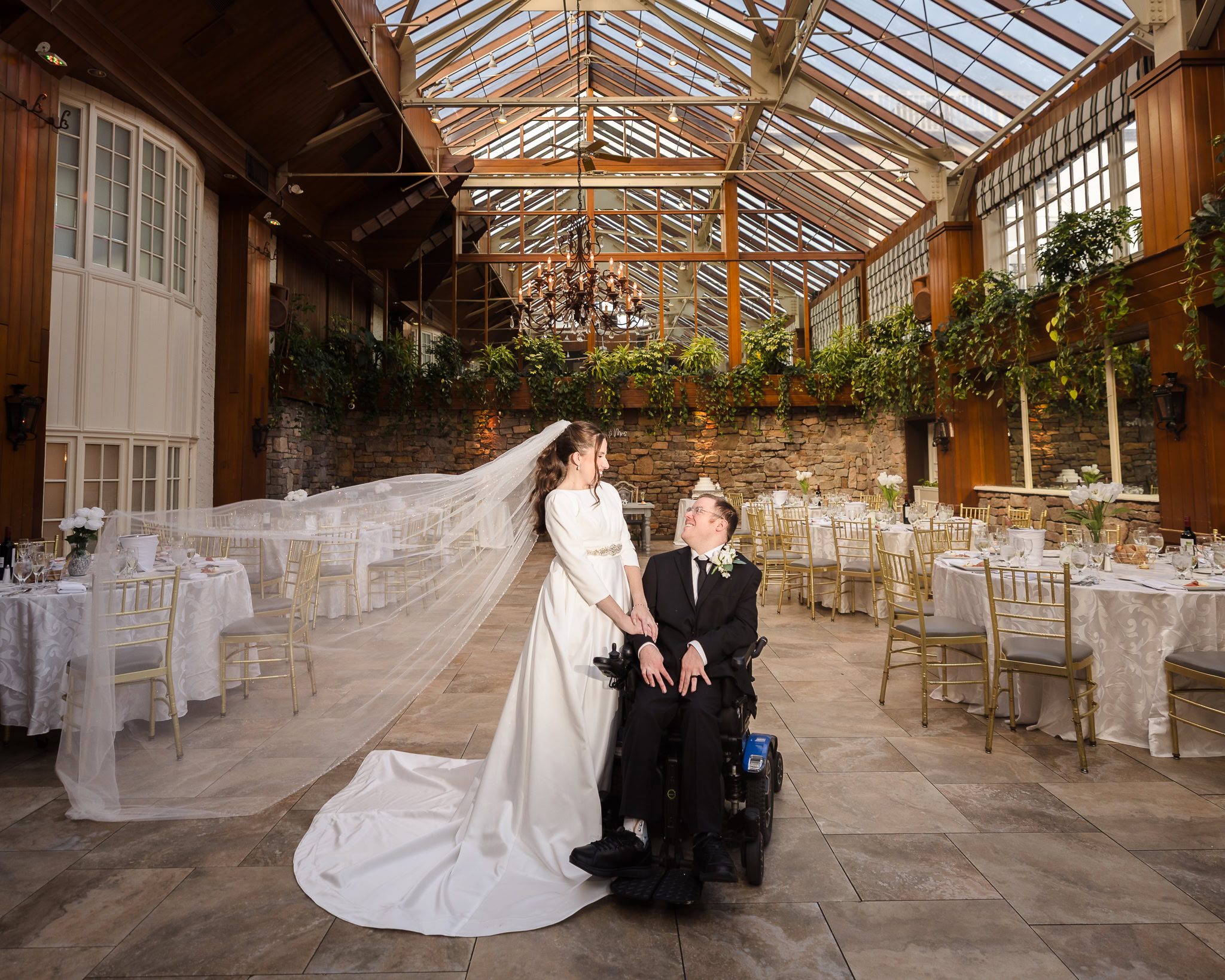Bride and groom share a joyful moment beneath the glass ceiling of the Fox Hollow Winter Garden, surrounded by elegant reception décor and golden-hour light.