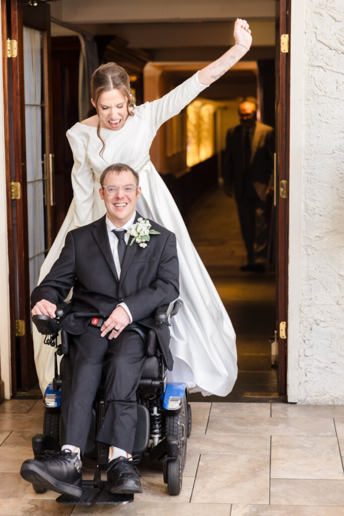 Bride and groom enter the reception space with wide smiles, bride raising her arm in excitement.