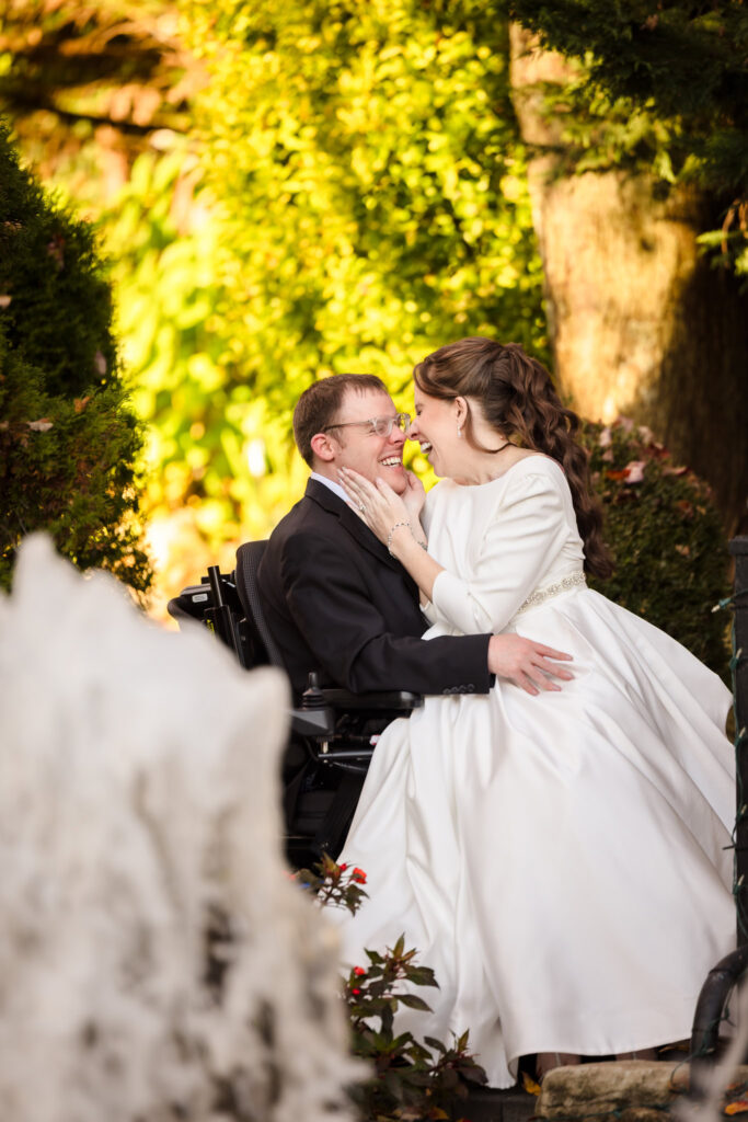 Bride sits on groom’s lap, laughing as they gaze at each other under fall trees at Fox Hollow.