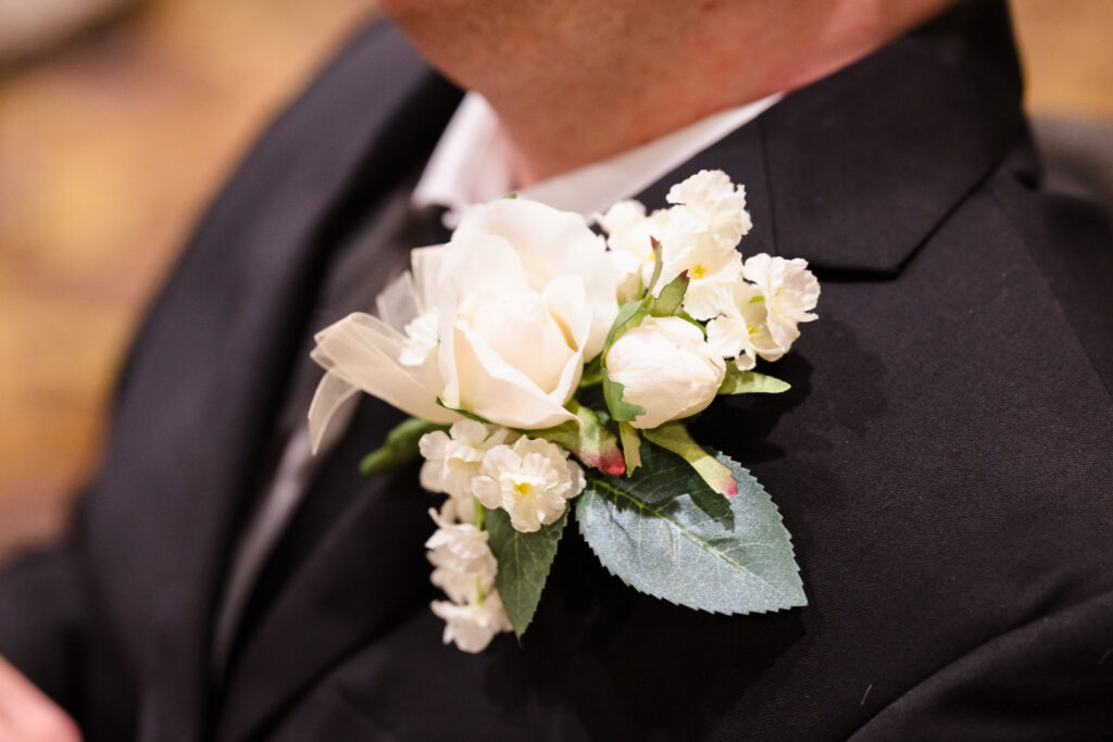 Detailed view of the groom’s white rose boutonniere accented with greenery and baby’s breath.