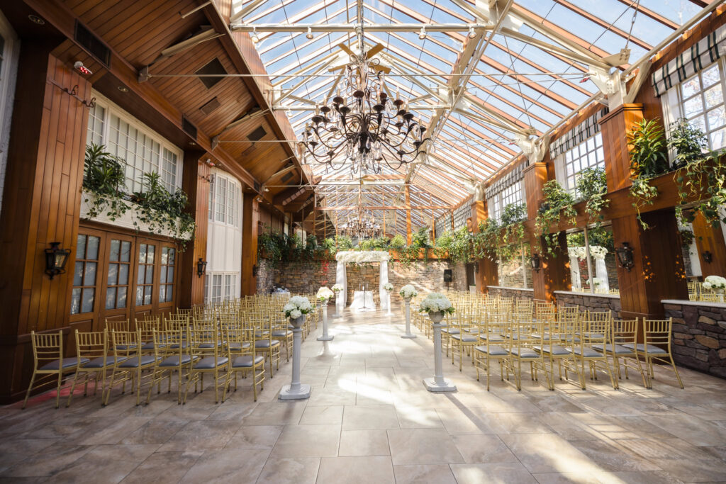 Indoor ceremony space at Fox Hollow’s Winter Garden with gold chairs, white florals, and a sunlit glass ceiling.
