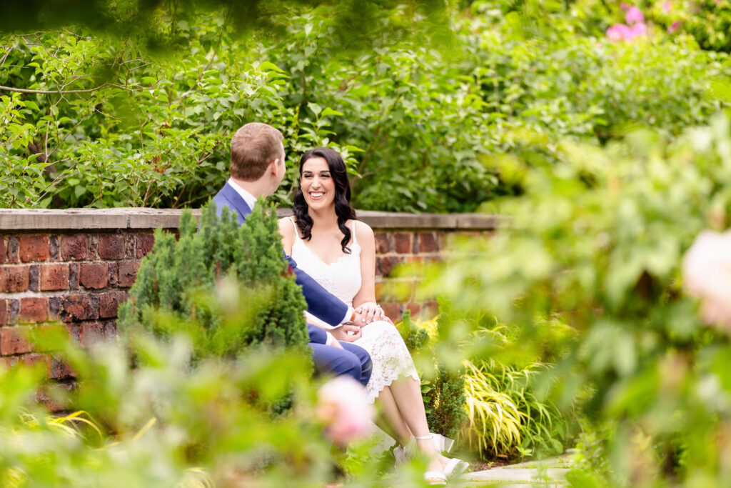 Christine and Bill sharing a joyful moment on a garden bench at Planting Fields Arboretum during their spring engagement session in Long Island, NY