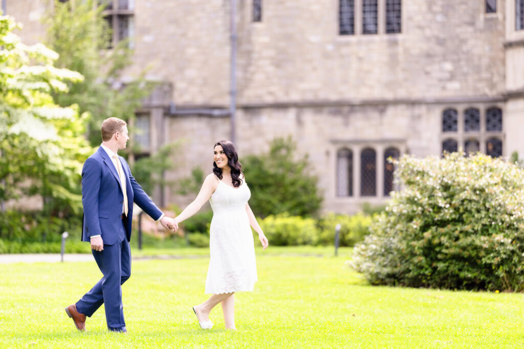 Christine and Bill walking hand-in-hand on the lawn at Planting Fields Arboretum, surrounded by lush greenery and historic architecture during their Long Island engagement session
