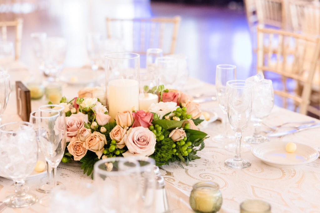 A soft, romantic tablescape at The Heritage Club at Bethpage featuring blush and mauve roses, lush greenery, and glowing candles—setting the tone for an evening of timeless celebration and refined beauty.