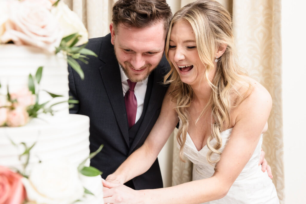 The bride and groom share a joyful laugh as they cut their wedding cake together at The Heritage Club at Bethpage—a sweet, lighthearted moment of connection and celebration.