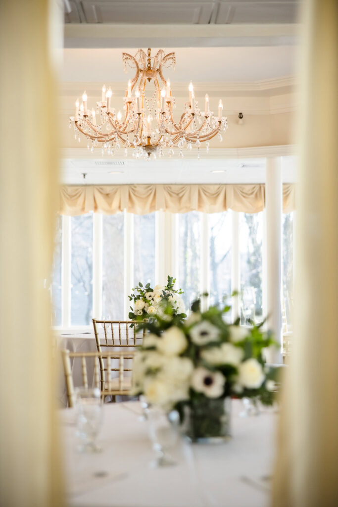 Elegant floral centerpiece beneath a crystal chandelier in a softly lit room with bay windows at Sea Cliff Manor.
