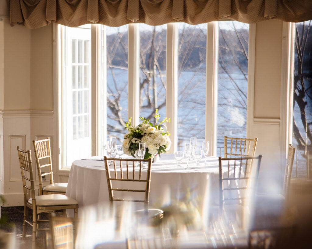 Intimate sweetheart table set for two with floral centerpiece and waterfront views through grand windows at Sea Cliff Manor.