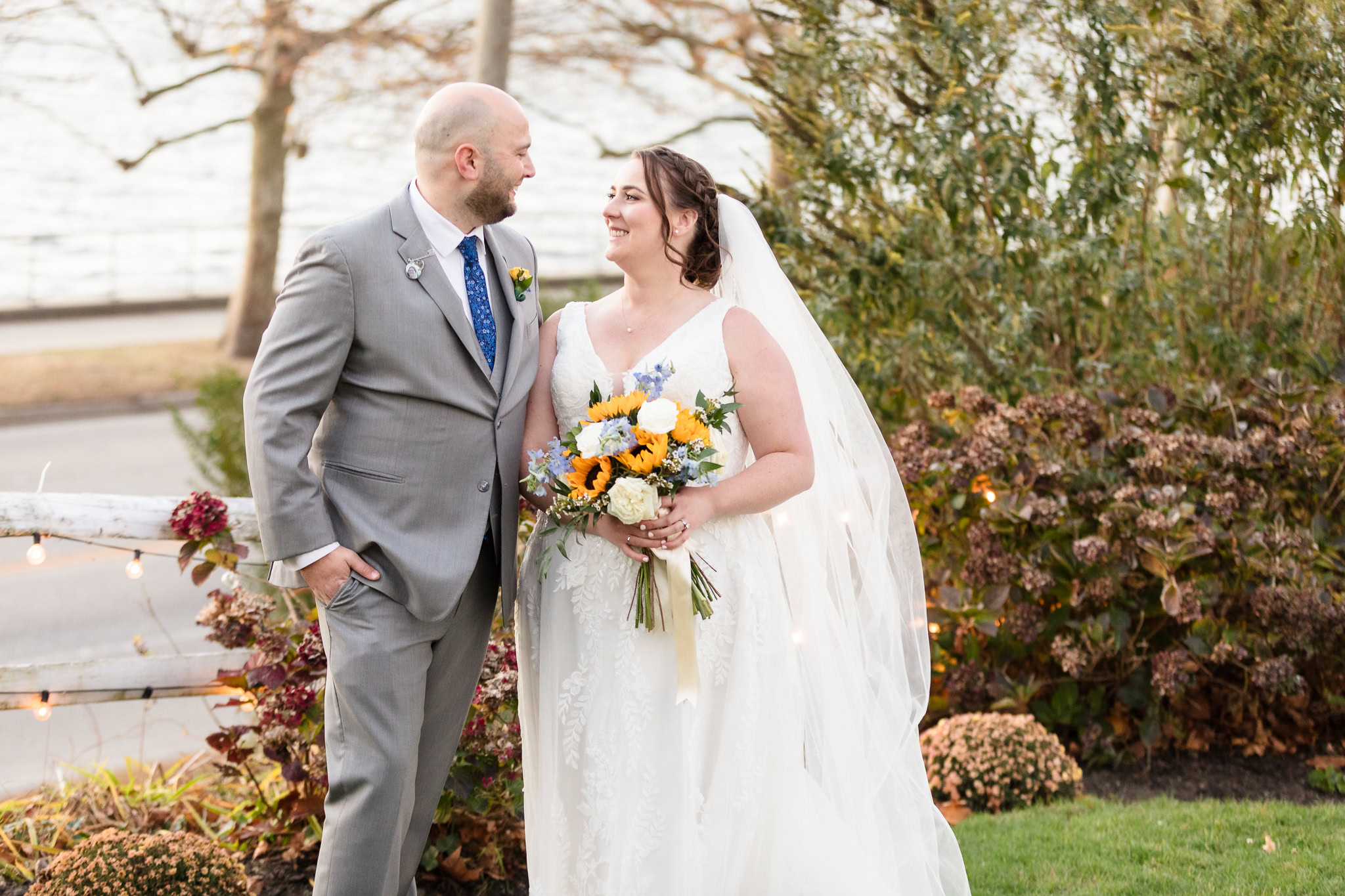 Bride and groom share a joyful moment in the garden at Sea Cliff Manor, with autumn florals and waterfront views in the background.