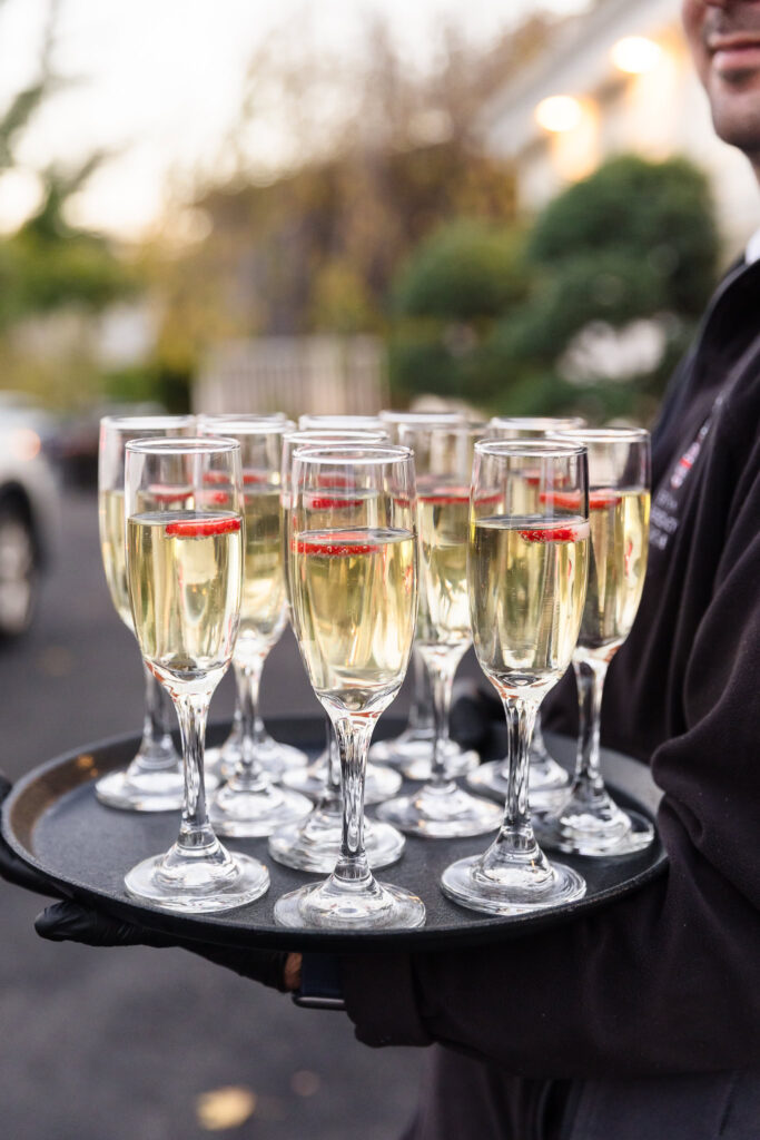 Tray of champagne flutes garnished with berries, offered to arriving wedding guests during cocktail hour at Sea Cliff Manor.