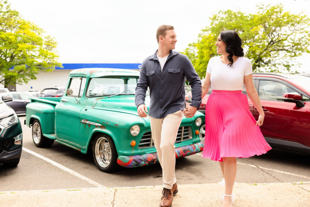 Engaged couple Christine and Bill walking hand-in-hand past a vintage turquoise pickup truck near Sugarberry café in Rockville Centre during their engagement session