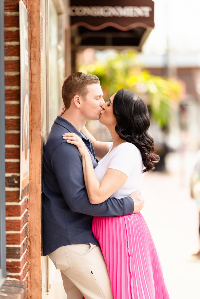 Christine and Bill sharing a romantic kiss outside a brick storefront in downtown Rockville Centre during their spring engagement session