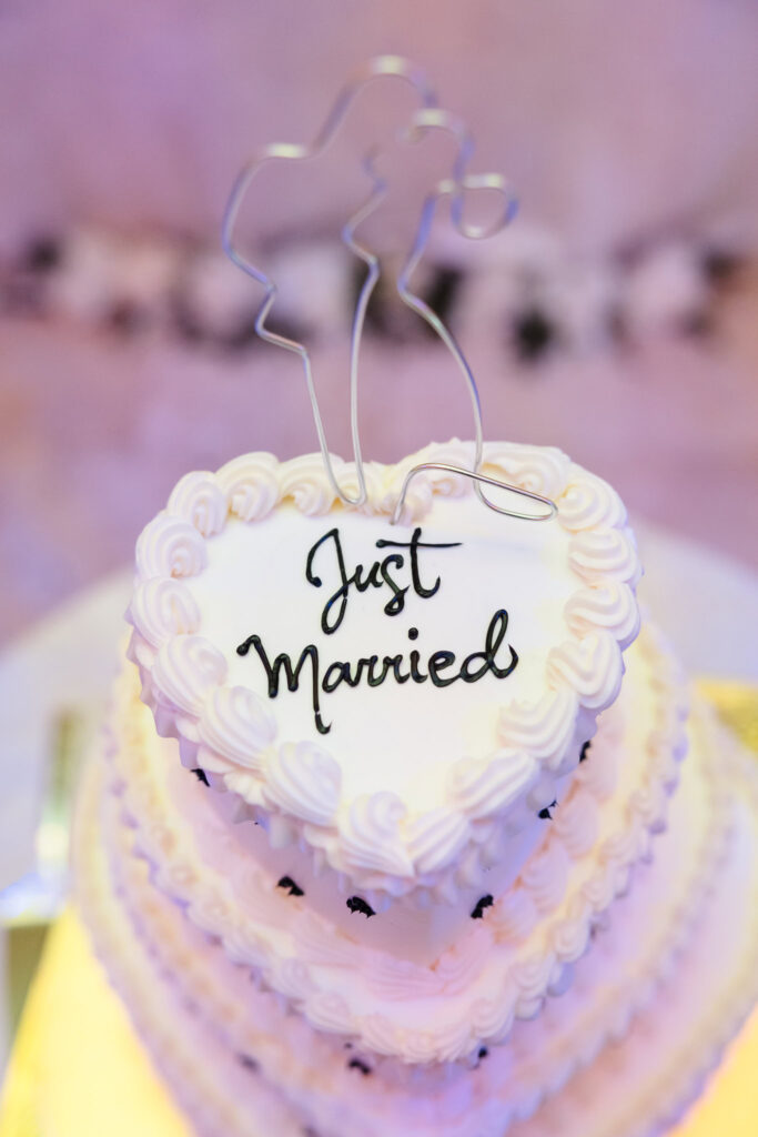 Heart-shaped wedding cake with white frosting and a “Just Married” topper, styled with elegant piping and a minimalist wire silhouette at The Inn at New Hyde Park.

