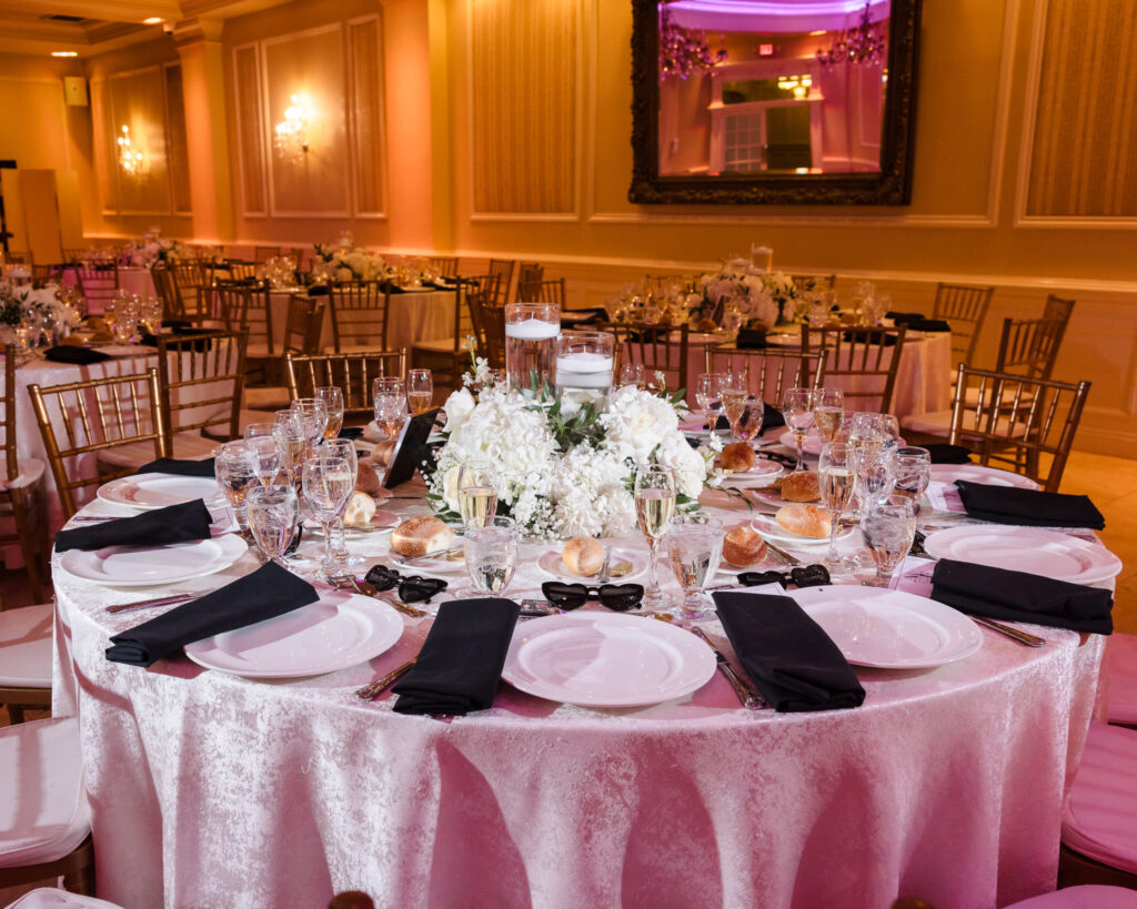 Elegant round wedding reception table set with black napkins, crystal glassware, and a lush white floral centerpiece at The Inn at New Hyde Park.

