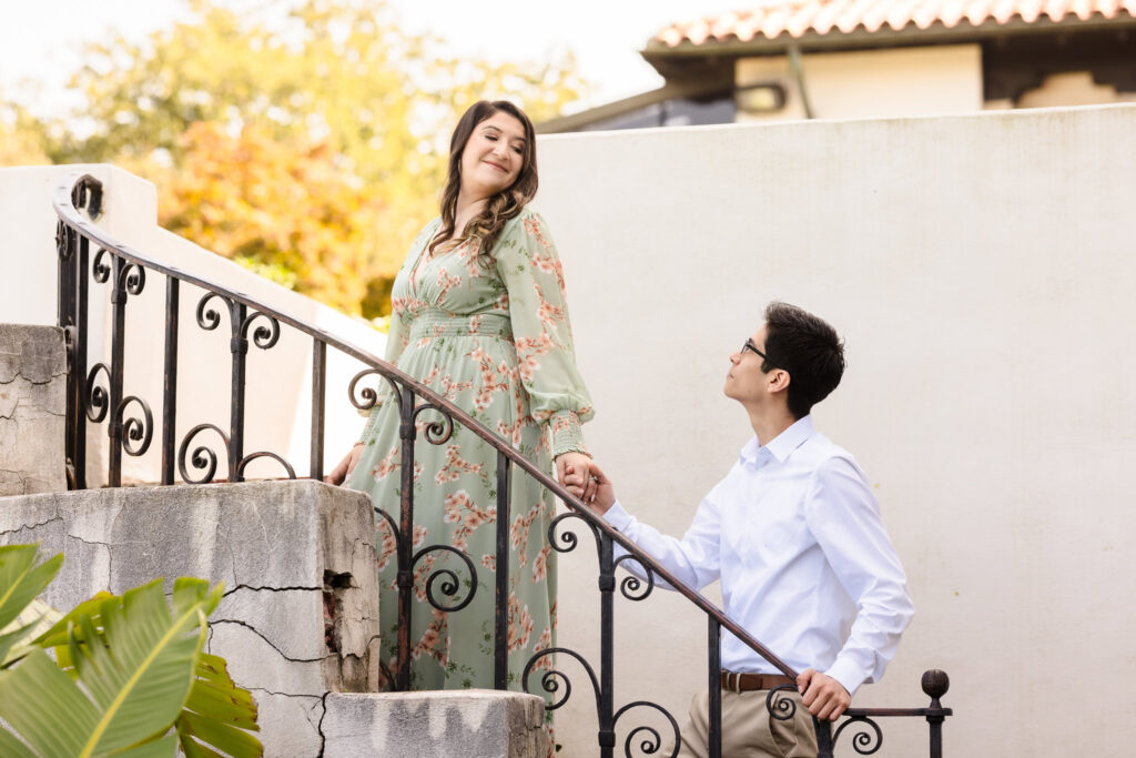 Groom-to-be admiring his fiancée as she leads him up the stone staircase at the Vanderbilt Museum, surrounded by autumn tones and historic architecture.