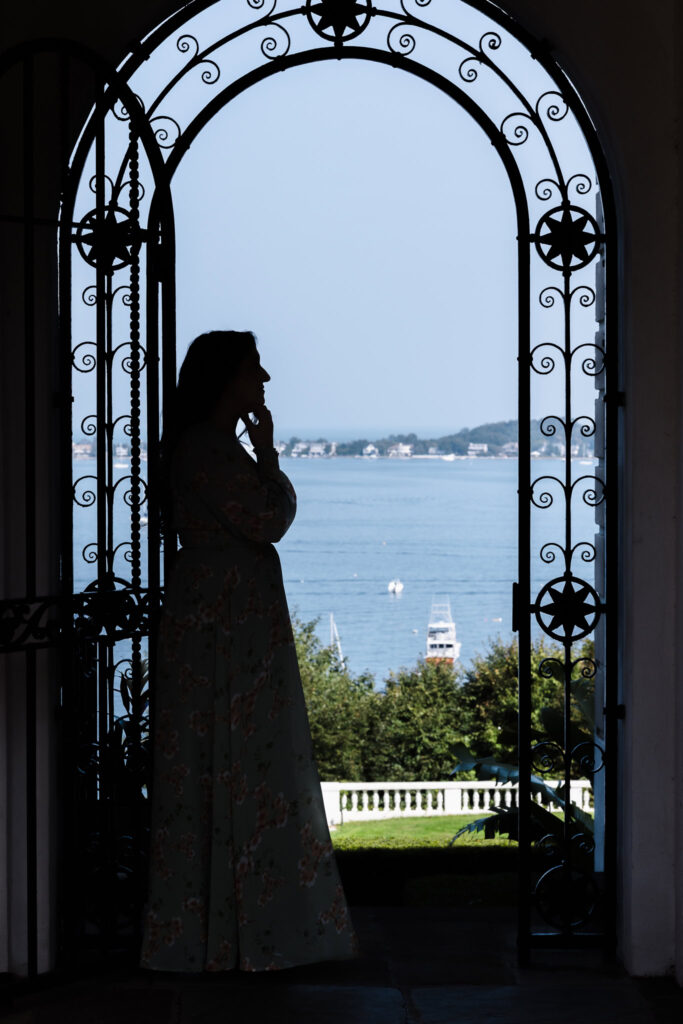 Silhouette of a woman standing in quiet reflection beneath an ornate archway at the Vanderbilt Museum, overlooking the still waters of the Long Island Sound.