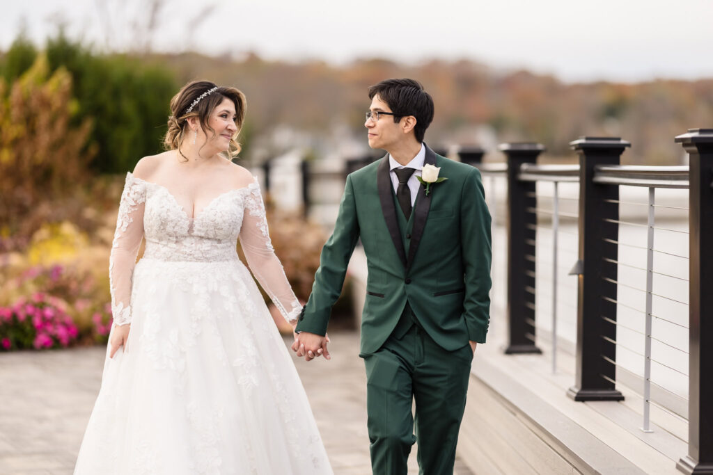 Bride and groom walk hand-in-hand along the waterfront deck at Water’s Edge Centerport on their wedding day.